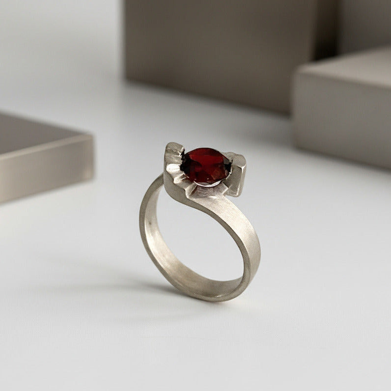 Un solitaire contemporain aux lignes architecturales, inspiré des escaliers en colimaçon. En argent brossé serti d'un grenat facetté, la bague Pas de Deux est signée Lucien Grandval.