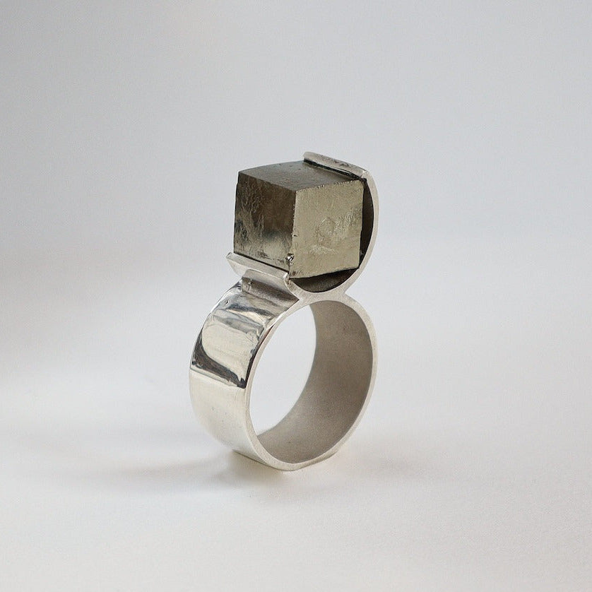 Bague O en argent poli, le design circulaire enlace une pyrite brute. Une création contemporaine signée Atellier Grandval.