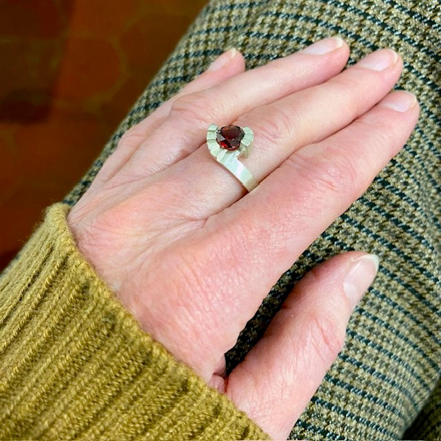 Bague Pas de Deux en argent brossé, sertie d’un grenat facetté. Un bijou contemporain sculptural inspiré des escaliers en colimaçon. Bijou porté.