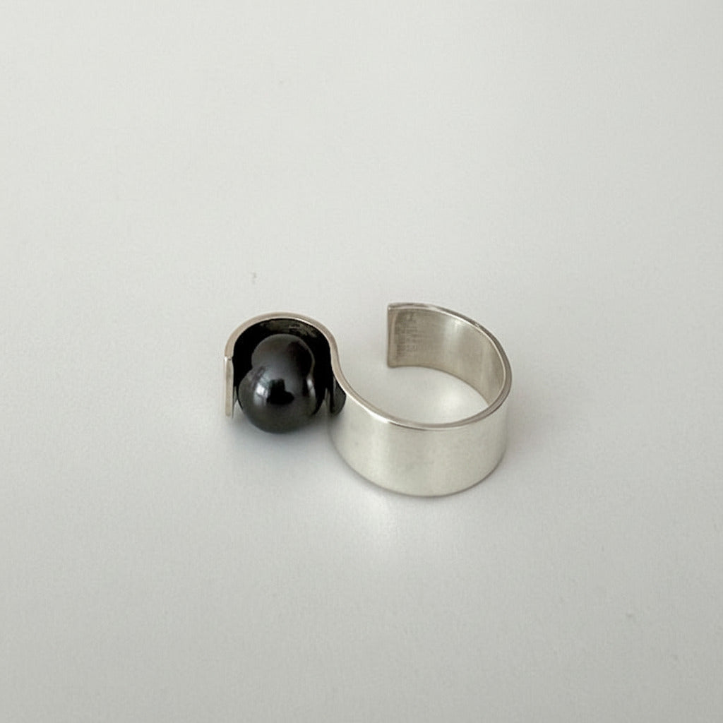 Bague ouverte en argent brossé et pli, son design minimaliste accueille une perle de Tahiti noire.