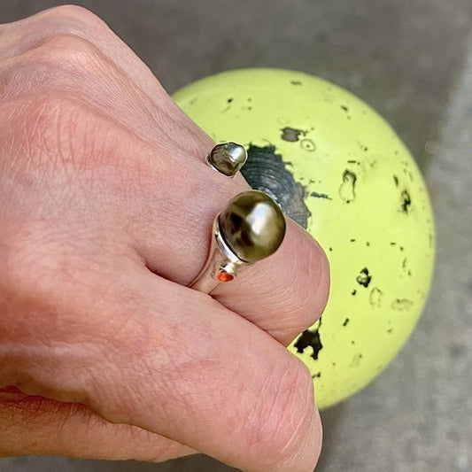 Bague ouverte forme "Toi et Moi" en argent avec d'un côté une perle keishi et de l'autre une perle tahitienne au reflet vert ornée d'une opale orange du Mexique. 
