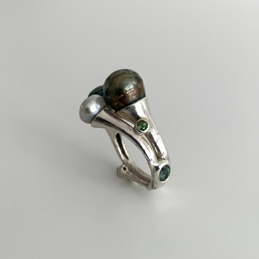 Cette bague ouverte, façonnée en argent ciselé, met en scène trois perles singulières : deux perles de Tahiti sculptées aux reflets changeants et une perle keshi. Une bague contemporaine, élégante et délicate réalisée à la main en pièce unique.