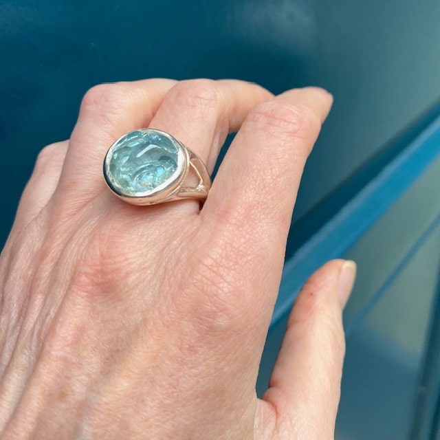 Bague argent sertie d'une aigue-marine forme cabochon . La pierre sculptée dissimule une opale révélant des reflets changeant. Son anneau en argent ciselé présente deux aigues-marines facettées.