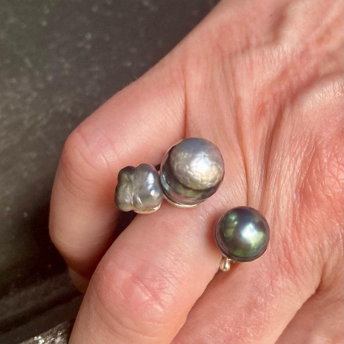 Bague ouverte présentant deux perles de Tahiti  sculptée,de couleurs différentes. L'anneau en argent est orné de petites pierres de couleurs.