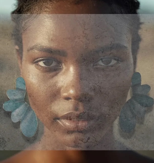 Boucles d'oreilles bleu clair en bronze laminé et peintes à la main, en forme de demi-fleur minimaliste, légère et aérienne. Bijou porté.