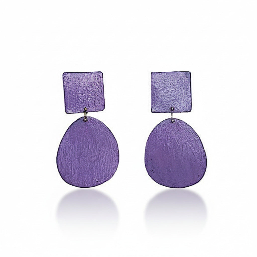 Réalisées en bronze laminé, ces boucles d’oreilles étonnent par leur légèreté. Elles présentent un élément ovale suspendu à un élément carré placé sur l’oreille, composant une silhouette géométrique contemporaine à la présence sculpturale. La surface est peinte à la main avec des pigment acrylique violet.