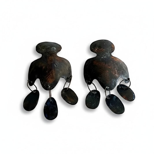 Cette paire en bronze laminé et pigments acryliques brun et noir se distingue par une découpe aux lignes arrondies et de trois pampilles allongées, alliant minimalisme et inspiration historique. Bijou façonné à la main par la créatrice greque Dora Haralembaki.