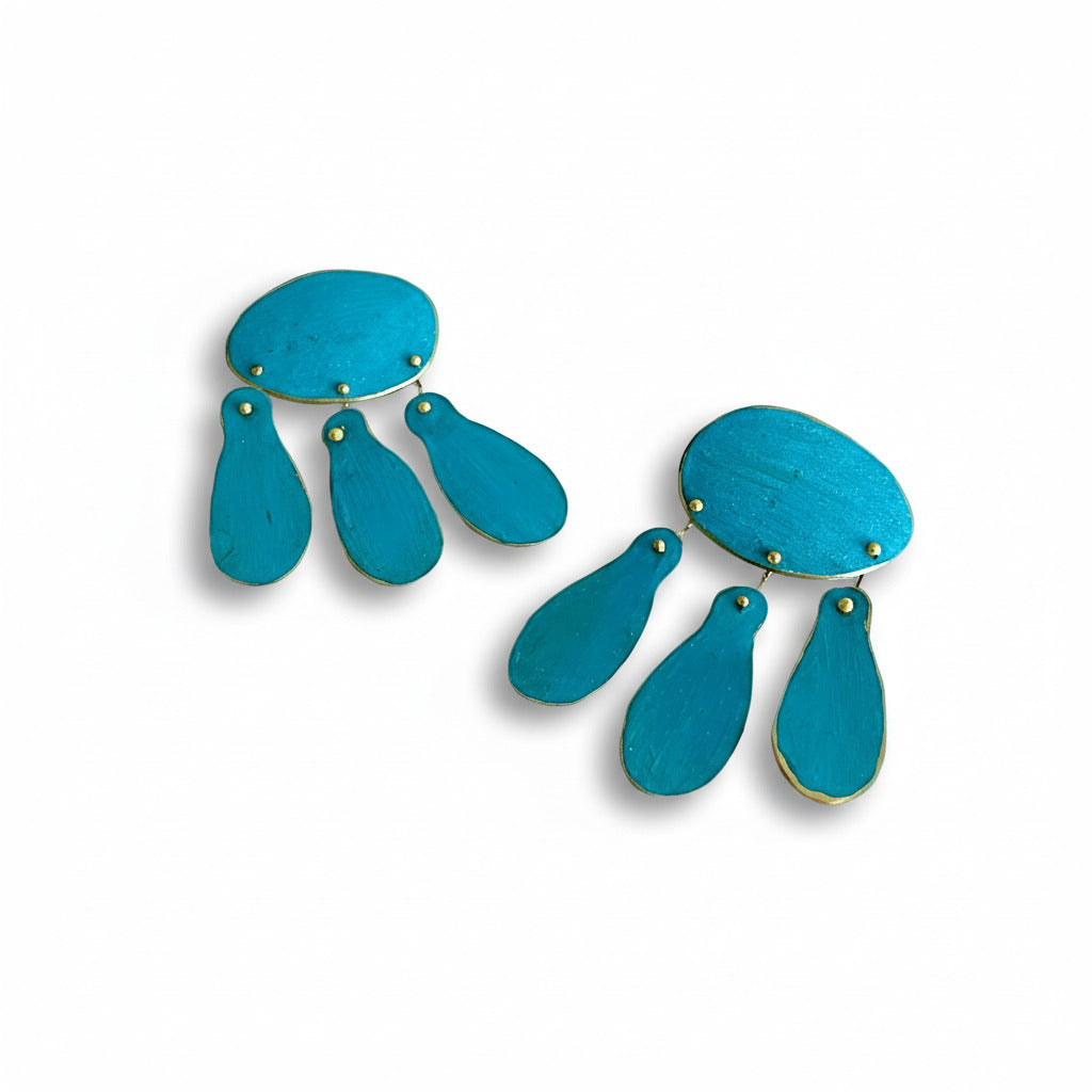 Composée d’un ovale et de trois pampilles allongées, cette paire de boucles d'oreilles réinterprète les bijoux du XIIIe siècle. Composées en bronze laminé , elles sont peintes à la main avec des pigments acryliques bleu turquoise.