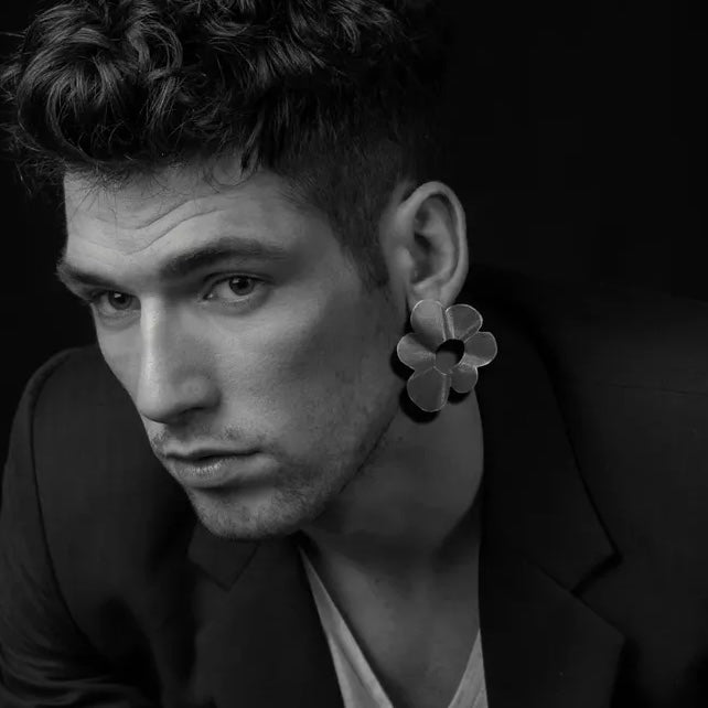 Boucles d'oreilles en bronze peintes avec des pygments acrylique mordoré, présentant une grande fleur stylisée. Un design contemporain réalisé par la créatrice grecque Dora Haralambaki. Bijoux porté par un homme vue de proil.