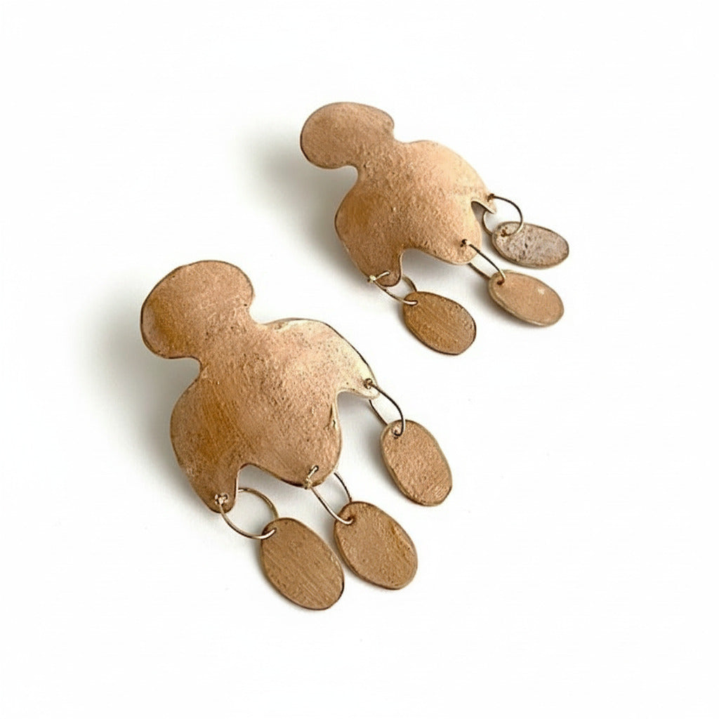 Cette paire en bronze laminé et peint avec des pigments beige se distingue par une découpe aux lignes arrondies et de trois pampilles allongées, alliant minimalisme et inspiration historique.