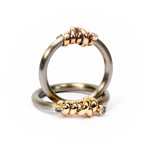 Anneau en acier poli, entrelacé d'une torsade d'or jaune ornée d'un zircon à chaque extrémité.