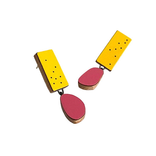 Boucles d'oreilles géométrique composées d'un élément ovale en formica fuchsia suspendu à un rectangle jaune d’or décoré de petits points noirs. Fabriquées en bois et formica, les deux éléments sont reliés par une attache en argent oxydé. Boucles d’oreilles légères et colorées faites main – Karen, artiste belge.
