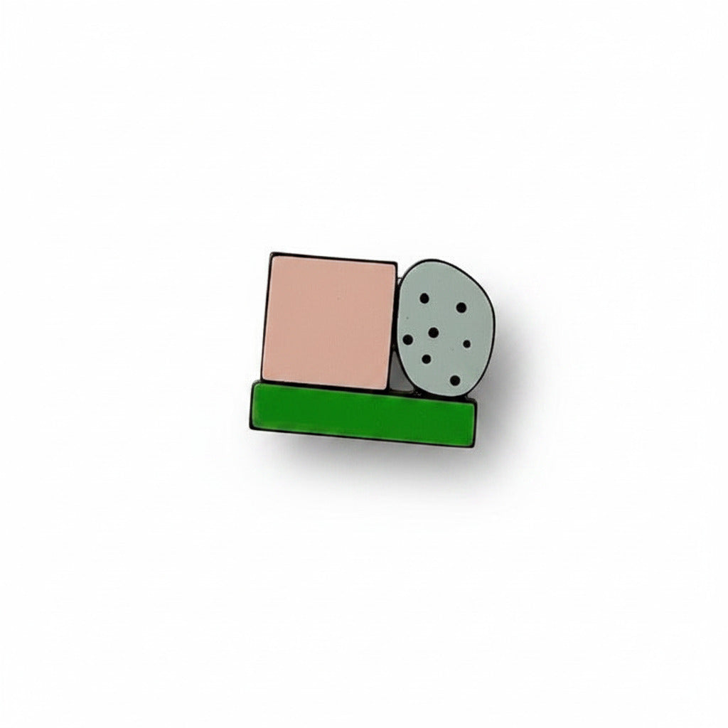 Cette mini broche en bois et Formica coloré assemble trois éléments géométriques : un rond gris ponctué de petits points, un carré rose poudré et un rectangle vert. 