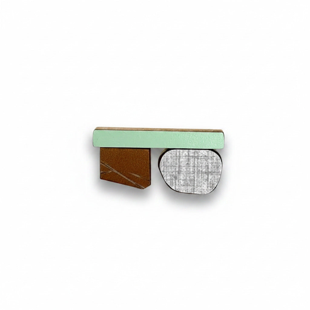 Mini broche moderne en bois avec composition graphique colorée. 3 éléments de bois recouvert de formica brun, vert clair et gris texturé. Pièce unique, création artisanale signée Karen Vanmol.
