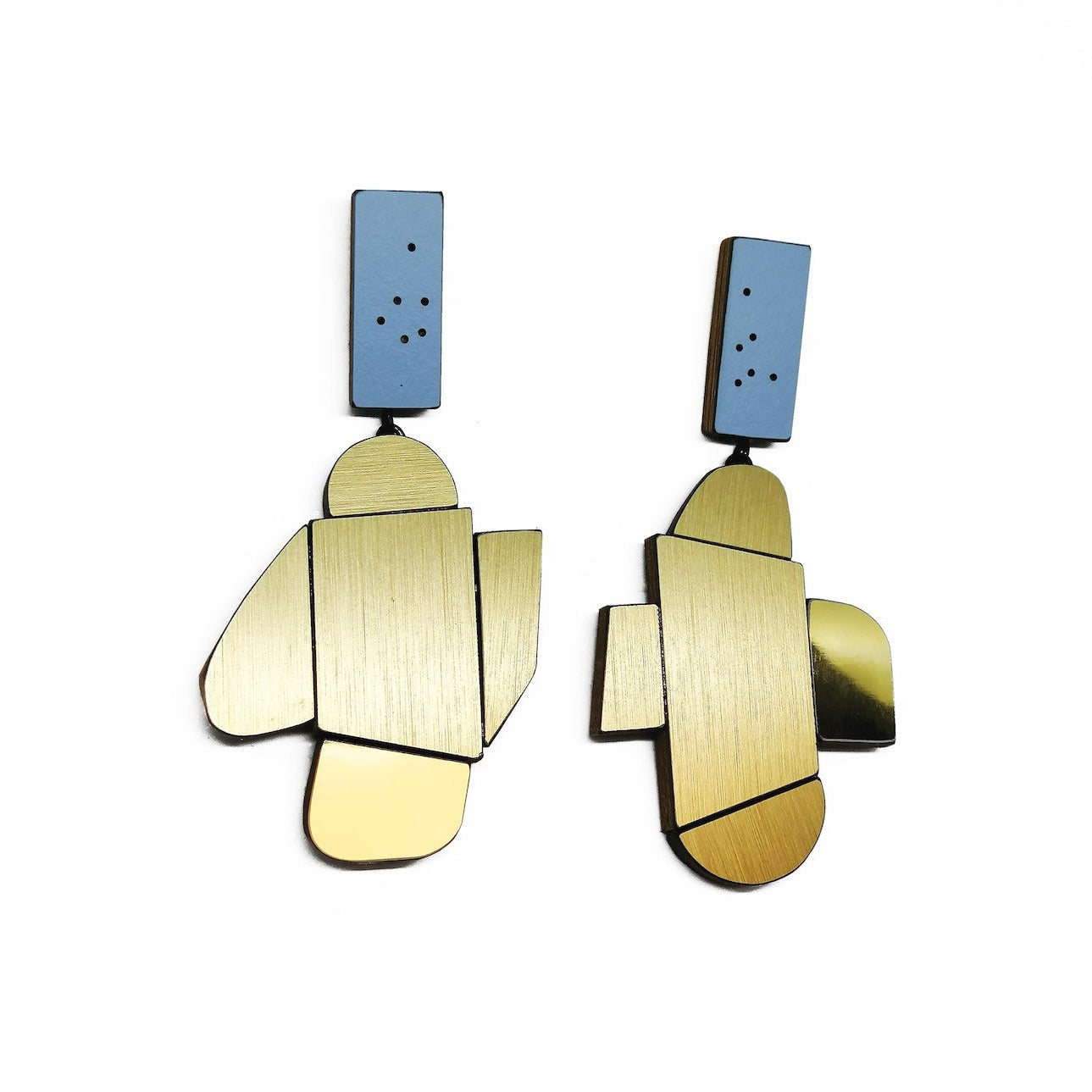 Suspendues à un support rectangulaire bleu clair à petits points noirs, ces boucles XL associent bois, formica doré texturé et doré métallisé. Légères et sculpturales, elles sont faites à la main par l’artiste belge Karen Vanmol.