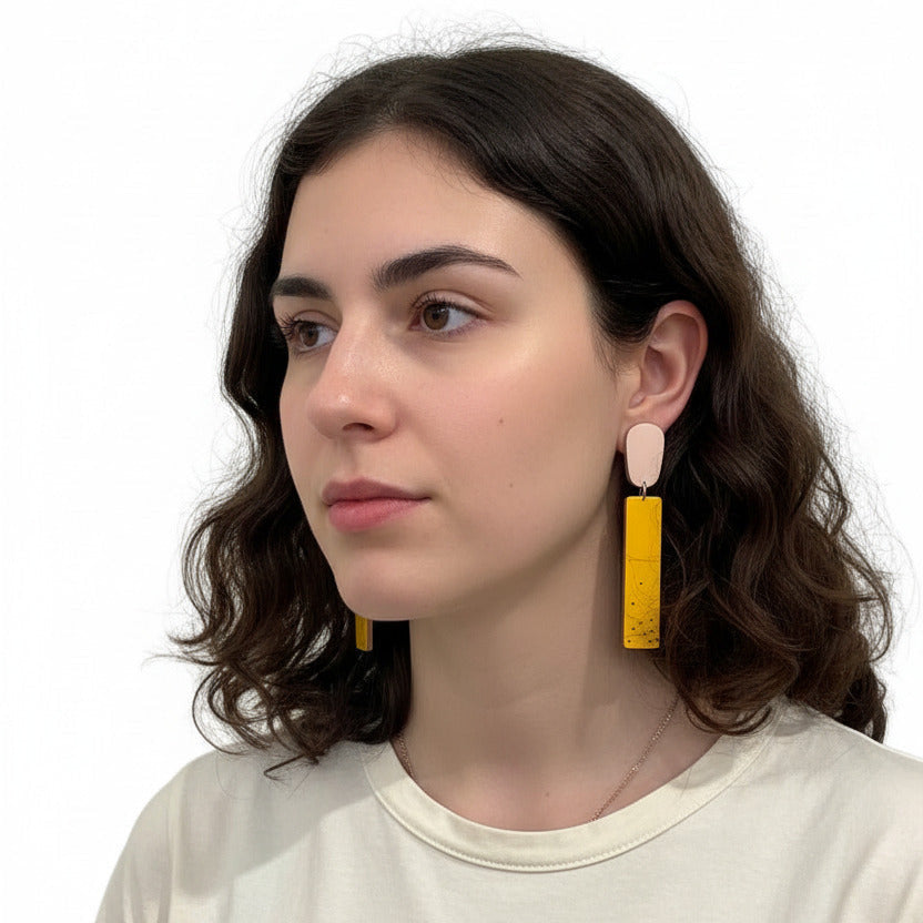 Boucles d’oreilles géométriques en bois et Formica rose et jaune d’or, finition mate et argent oxydé. Design contemporain léger et graphique. Bijoux portés.