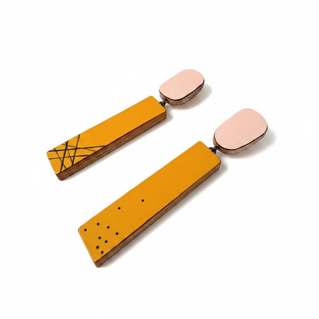Boucles d’oreilles géométriques en bois et Formica rose et jaune d’or, finition mate et argent oxydé. Chaque rectangle présente un motif singulier — l’un ponctué de petits points noirs, l’autre de lignes graphiques