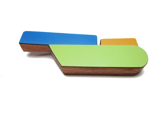 Broche contemporaine en bois et formica bleu, vert et ocre. Pièce unique réalisée à la main par l’artiste belge Karen, au design graphique et coloré. 