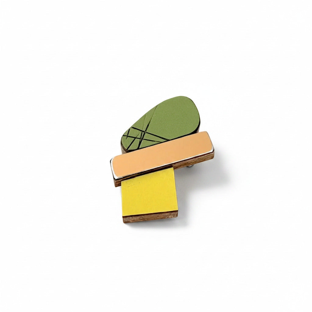 Mini broche graphique en bois et Formica associe trois éléments géométriques : un jaune lumineux, un kaki strié aux accents graphiques, et une finition métallisée effet miroir qui capte la lumière.