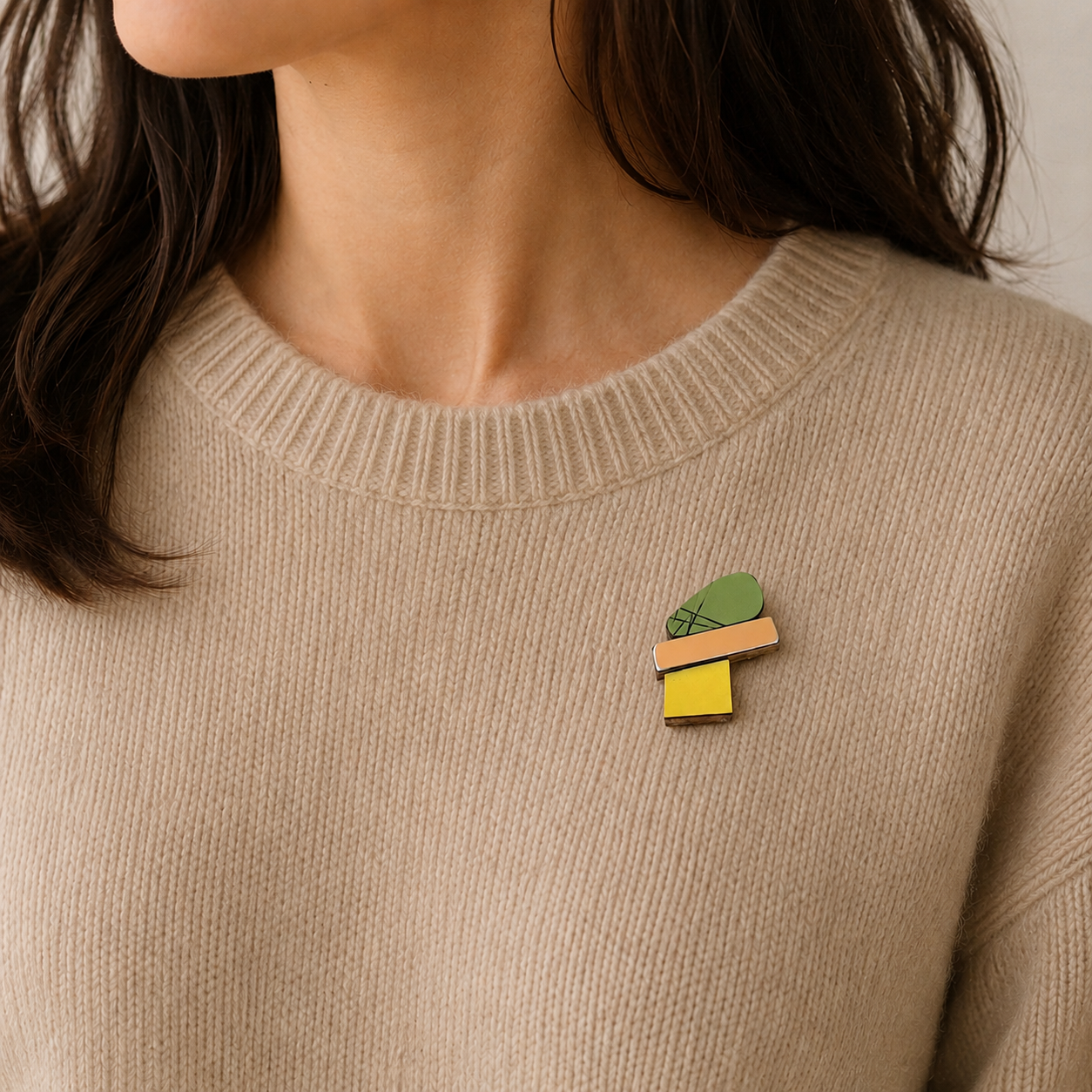 Mini broche contemporaine colorée avec finition métallisée et pin’s acier. Bijou porté sur un pull beige.