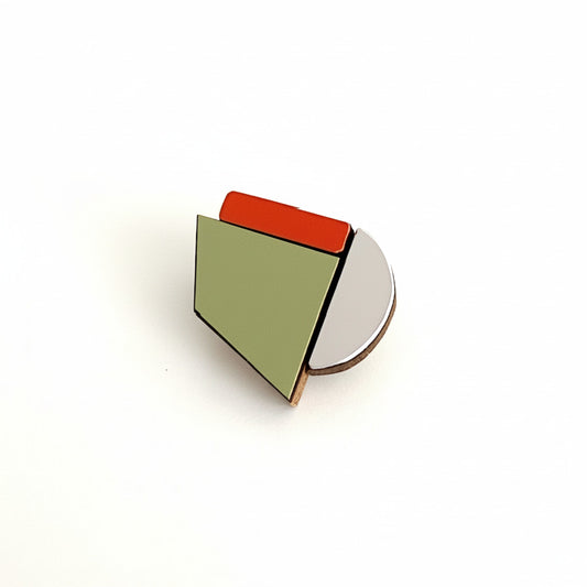 Petite broche graphique en bois et formica orange, kaki et argenté. Légère, ludique et faite main par l’artiste belge Karen. À porter seule ou en composition.