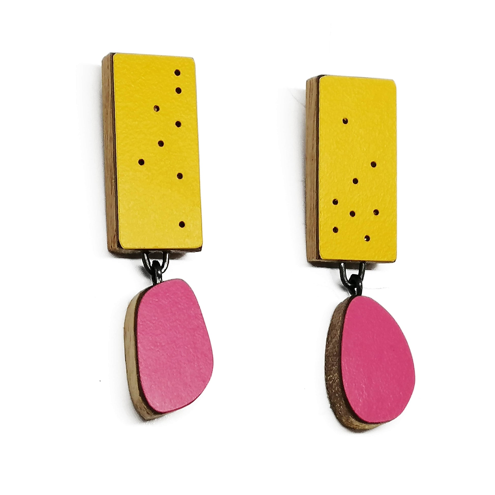 Boucles d'oreilles composées d'un élément ovale en formica fuchsia suspendu à un rectangle jaune d’or décoré de petits points noirs. Fabriquées en bois et formica, les deux éléments sont reliés par une attache en argent oxydé,