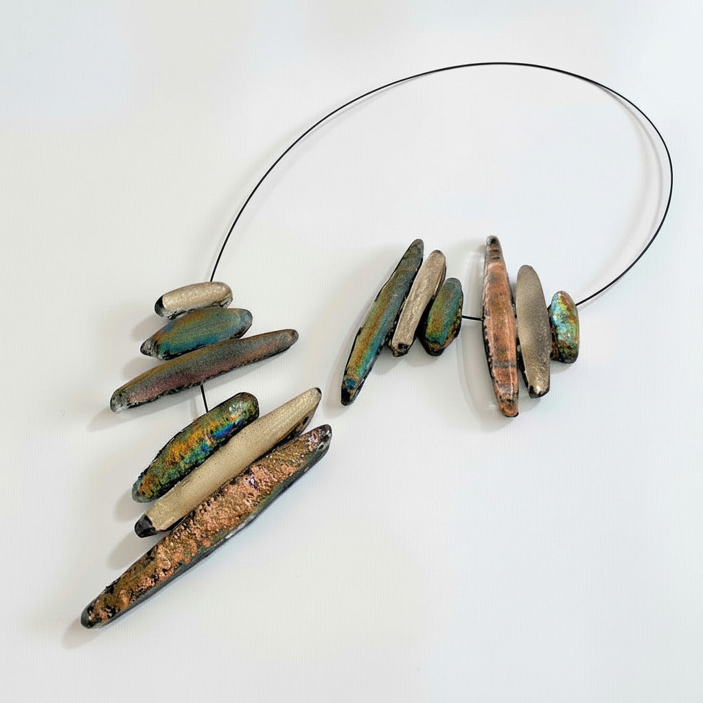 Collier sculptural en résine texturée composé de douze éléments en forme de stalactites dans des tonalités de beige rosé et de vert. Fermoir aimanté.