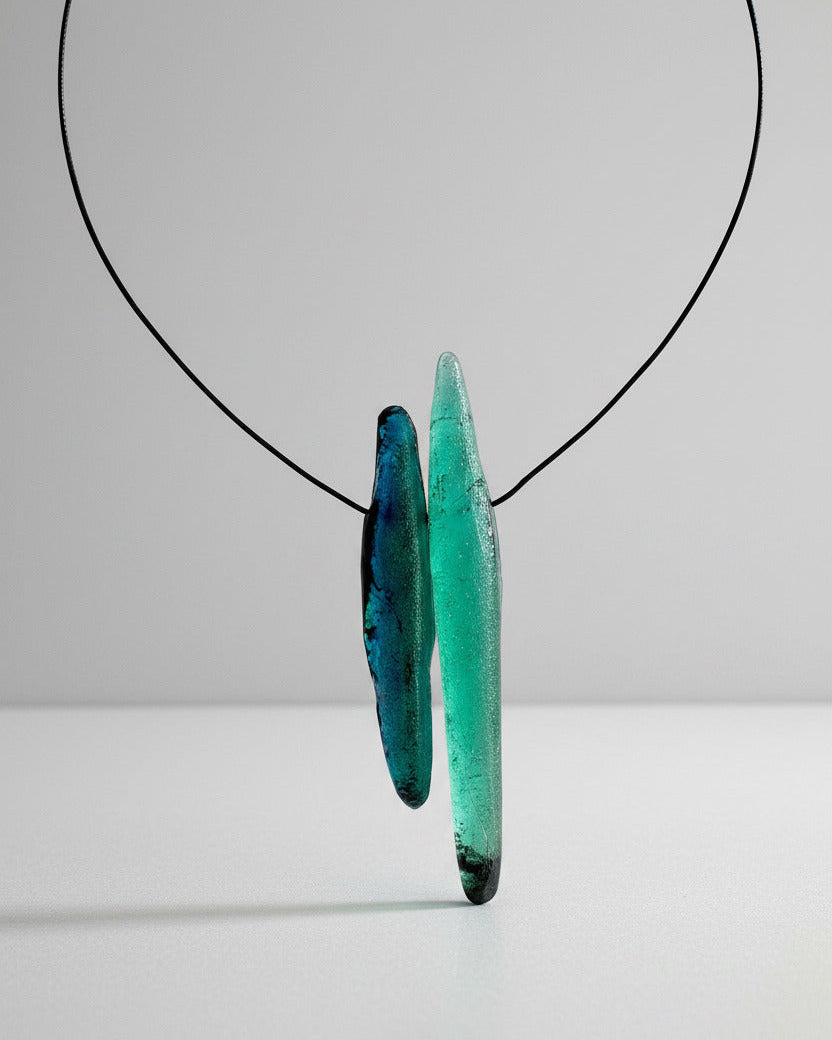 Ce collier contemporain et minimaliste présente deux éléments allongés en résine texturé sur Câble noir. L'un est vert émeraude, l'autre céladon. 