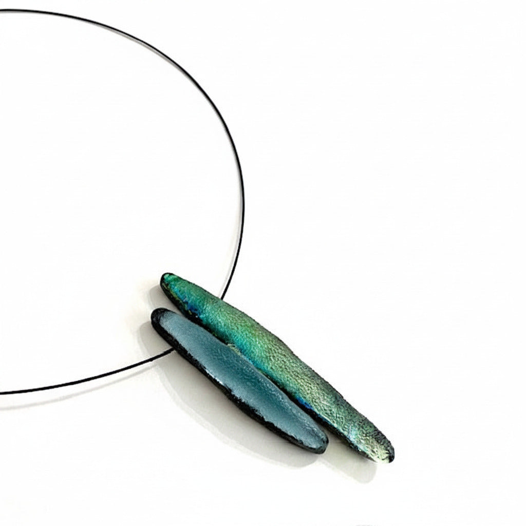 Collier graphique composé de deux éléments allongés en résine irisée verte et bleue sur câble noir. Bijou contemporain léger, réalisé artisanalement avec fermoir aimanté.