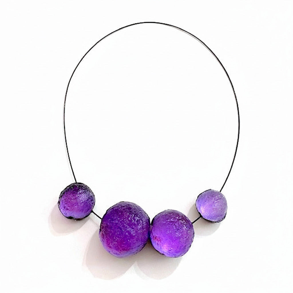 Collier contemporain composé de sphères en résine violette texturée sur câble noir. Fermoir aimanté intégré et design sculptural.