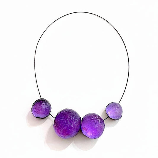 Collier contemporain composé de sphères en résine violette texturée sur câble noir. Fermoir aimanté intégré et design sculptural.
