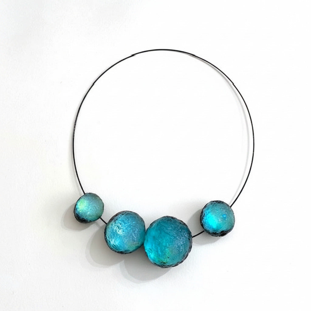 Collier contemporain composé de quatre sphères en résine turquoise texturée sur câble noir. Fermoir aimanté intégré et design sculptural.