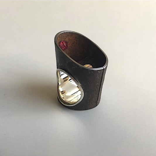 Bague haute et ovale en fer rouillé montée un large anneau douille en argent poli. Cachée de biais à l'intérieur de la bague, une tourmaline rose.