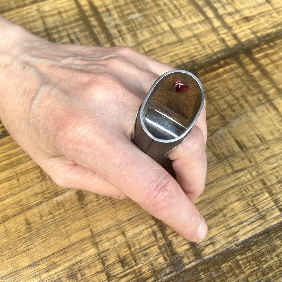 Bague haute et ovale en fer rouillé montée un large anneau douille en argent poli. À l'intérieur de la bague, sur le côté une tourmaline rose est cachée.