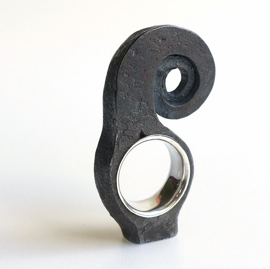 Bague haute en spirale, inspirée par la forme d'une feuille de fougère enroulée. Forgée dans du fer pur, cette forme aérienne repose sur un anneau large en argent. 