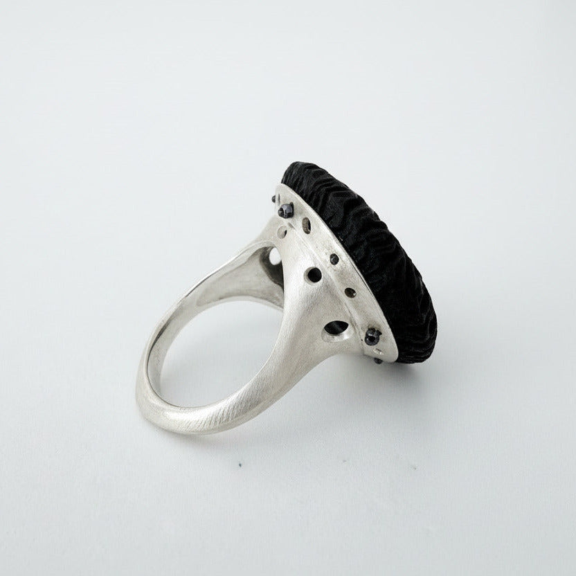 Bague contemporaine présentant un cabochon en ébène sculpté sur un corps de bague en argent satiné. Bijou de profil.