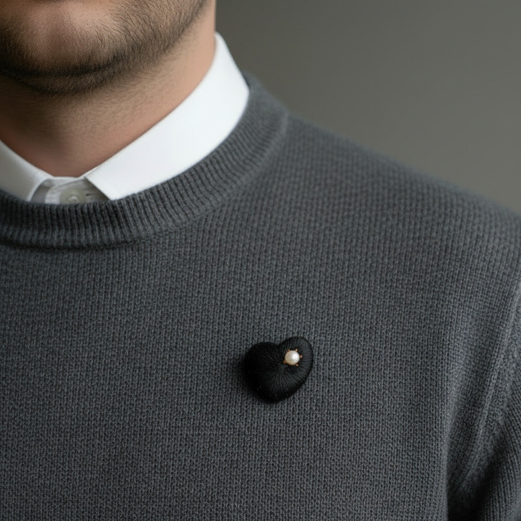 Broche en ébène sculpté et texturé orné d'une perle de culture blanche. Bijou fait main présenté sur un pull porté par un homme.