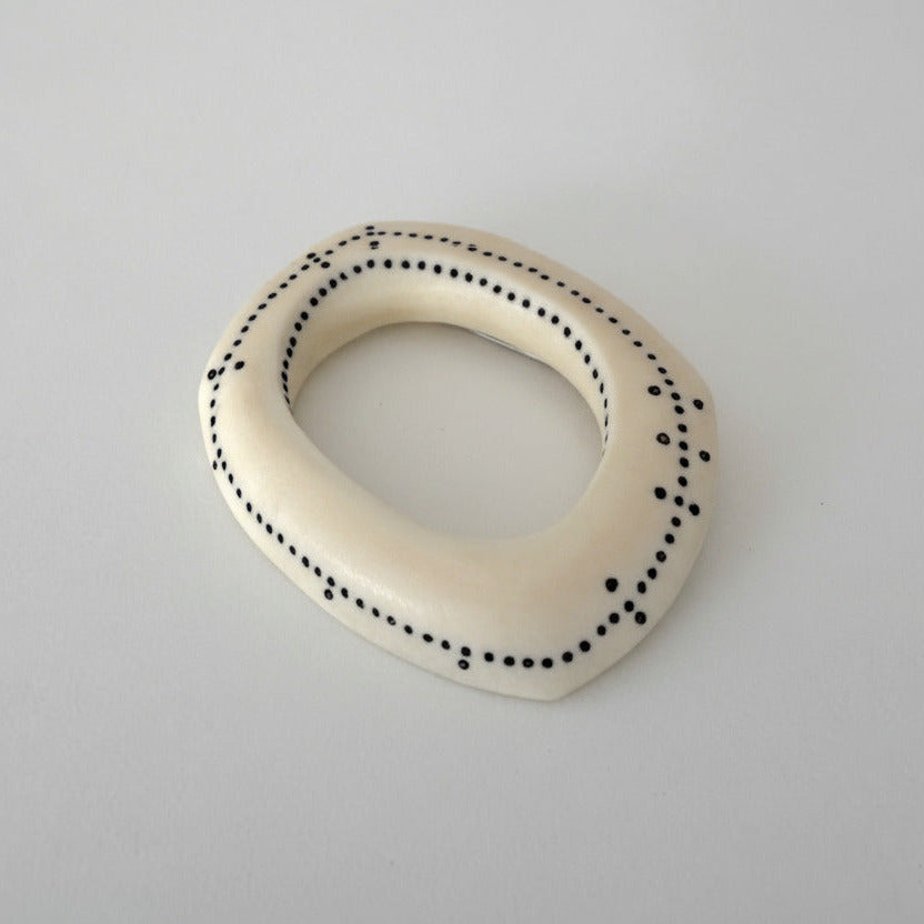 Broche en os sculpté décoré par un tracé de points noirs et quelques micro-perles de nylon noir, comme une ponctuation graphique.
