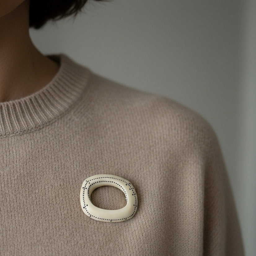 Broche géométrique en os sculpté et peint de petits points noirs en forme de lignes graphiques. Bijou porté sur un pull.