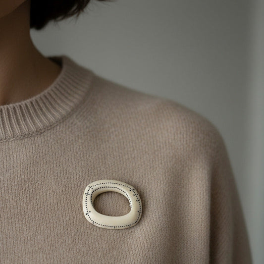 Broche géométrique en os sculpté et peint de petits points noirs en forme de lignes graphiques. Bijou porté sur un pull.