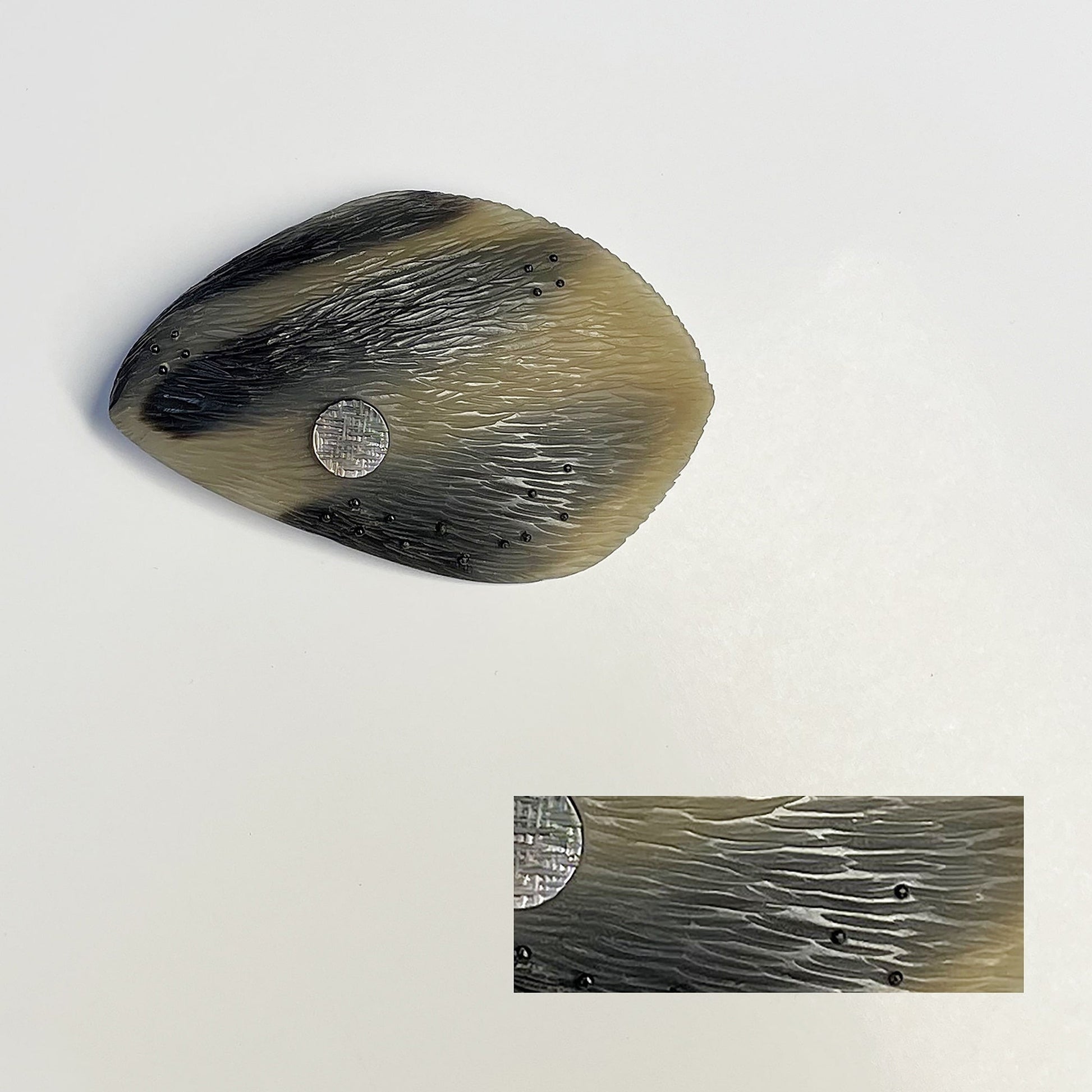 broche ovale, sculptée en corne dorée aux dessins bruns naturels. Le bijou est gravé, orné d'une pastille de nacre grise  et de fil de nylon perlé. Une pièce contemporaine réalisée à la main en pièce unique.