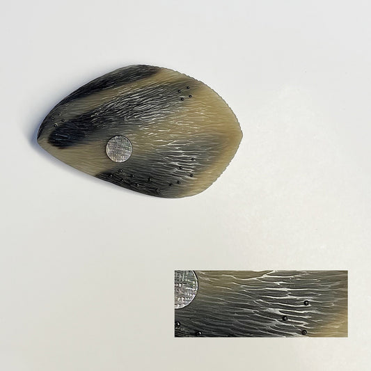 broche ovale, sculptée en corne dorée aux dessins bruns naturels. Le bijou est gravé, orné d'une pastille de nacre grise  et de fil de nylon perlé. Une pièce contemporaine réalisée à la main en pièce unique.