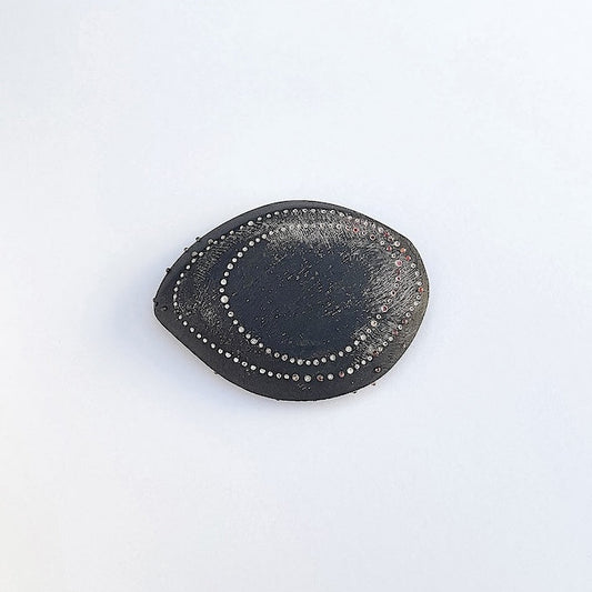 Cette broche en ébène sculpté, patiné et texturé révèle deux formes ovales dessinées par des points blancs et rosés peints à la main, rappelant l'esthétique des dessins aborigènes.