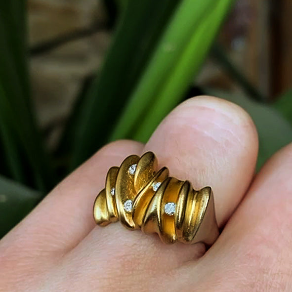 Une bague contemporaine en argent satiné aux courbes ondulées sublimées par un plaquage en or et sertie de 5 diamants. Détail du bijou porté.