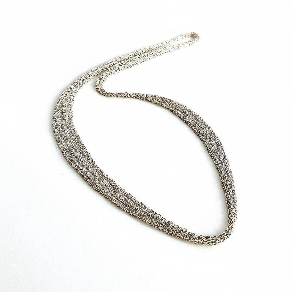 Collier en forme de ruban est composé de chaîne d'argent assemblée au fil de soie. Sans fermoir, ce collier s'enfile pas la tête, il est doux et confortable à porter. Une pièce moderne et délicate faite entièrement à la main par l'artiste Ria Lins.