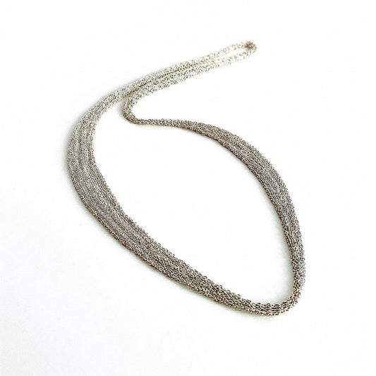Collier en forme de ruban est composé de chaîne d'argent assemblée au fil de soie. Sans fermoir, ce collier s'enfile pas la tête, il est doux et confortable à porter. Une pièce moderne et délicate faite entièrement à la main par l'artiste Ria Lins.