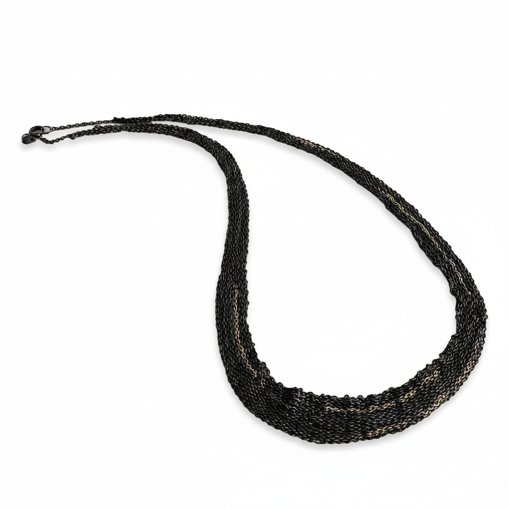 Collier léger et confortable en chaînes d'argent oxydé assemblées au fil de soie, avec des détails en chaîne dorée or rose. Un bijou fait main par l'artiste belge Ria Lins.