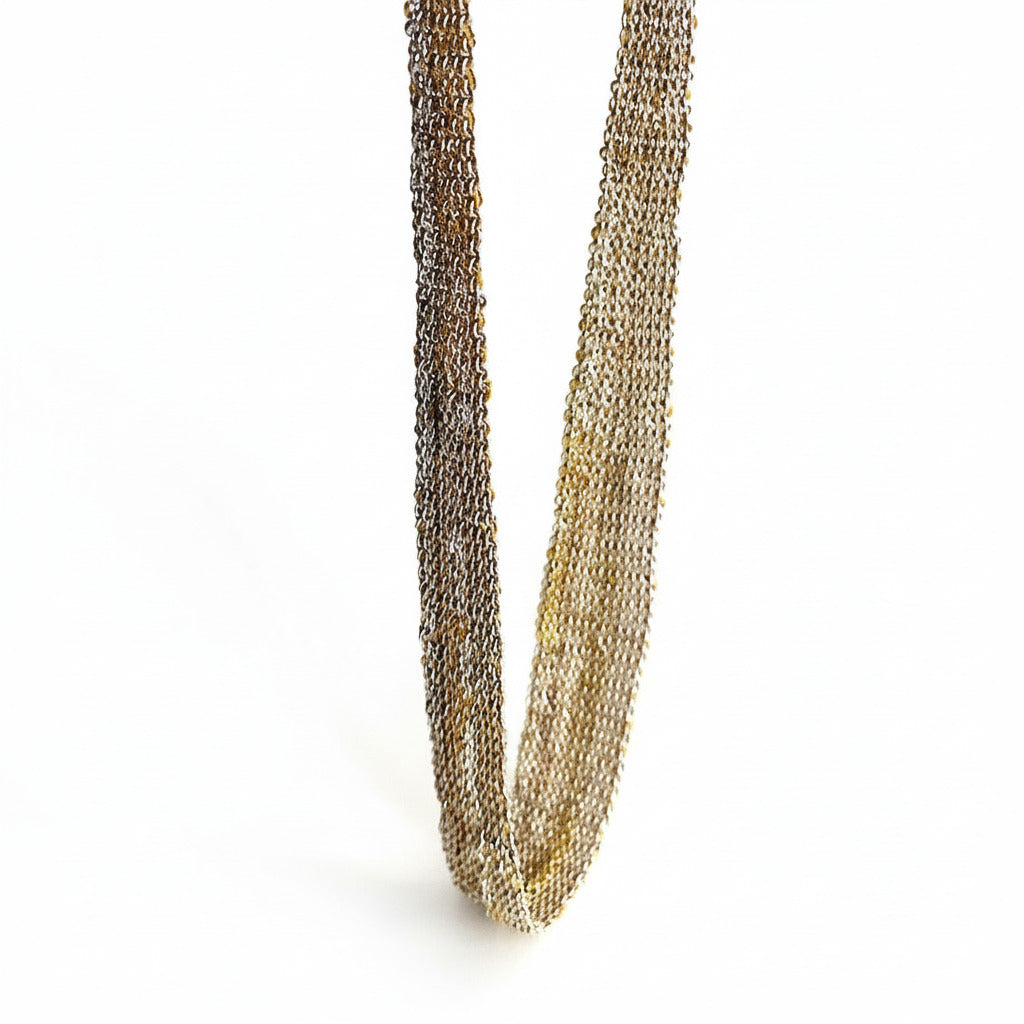 détail d'un tour de cou en forme de ruban dégradé, réalisé par un assemblage de chaînes d'argent et dorées au fil de soie. Un collier minimaliste fait main par l'artiste belge Ria Lins.