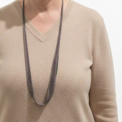 Sautoir composé de chaines en argent oxydé noir assemblées au fil de soie, orné de 20 mini perles d’agate verte cousue sur un côté du bijou. Bijou porté sur pull beige.