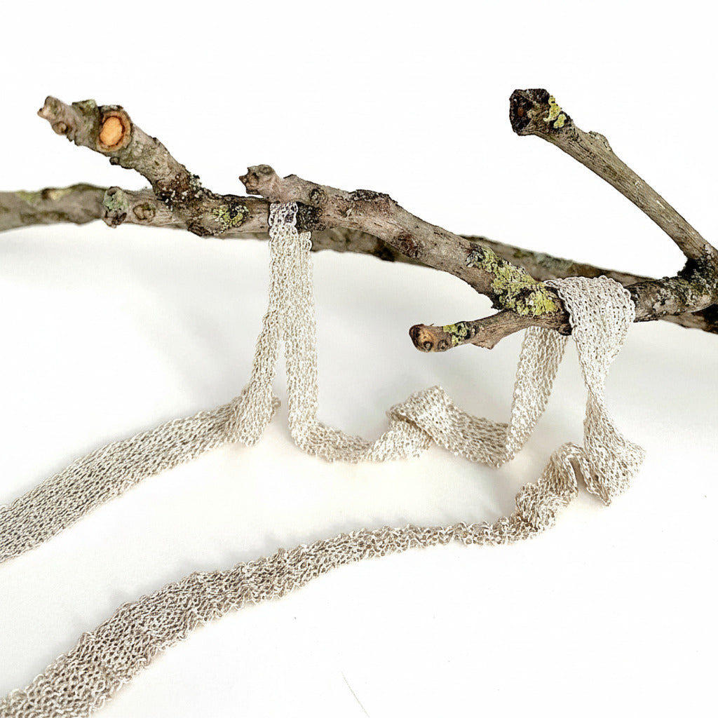 Ce collier moderne et délicat en forme de ruban est composé de chaîne d'argent assemblée au fil de soie. Sans fermoir. Bijoux présenté sur une branche d'arbre. Un bijou artisanal fait entièrement à la main par l'artiste Ria Lins?